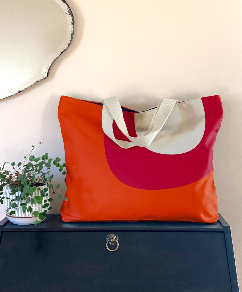 May include: Orange and red tote bag with white canvas straps. The bag has a geometric design with a large red semi-circle on the front.