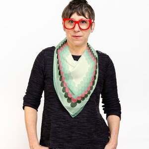 May include: A woman wearing a black sweater and black and white patterned pants. She is wearing a green, pink, and white patterned scarf and red glasses.