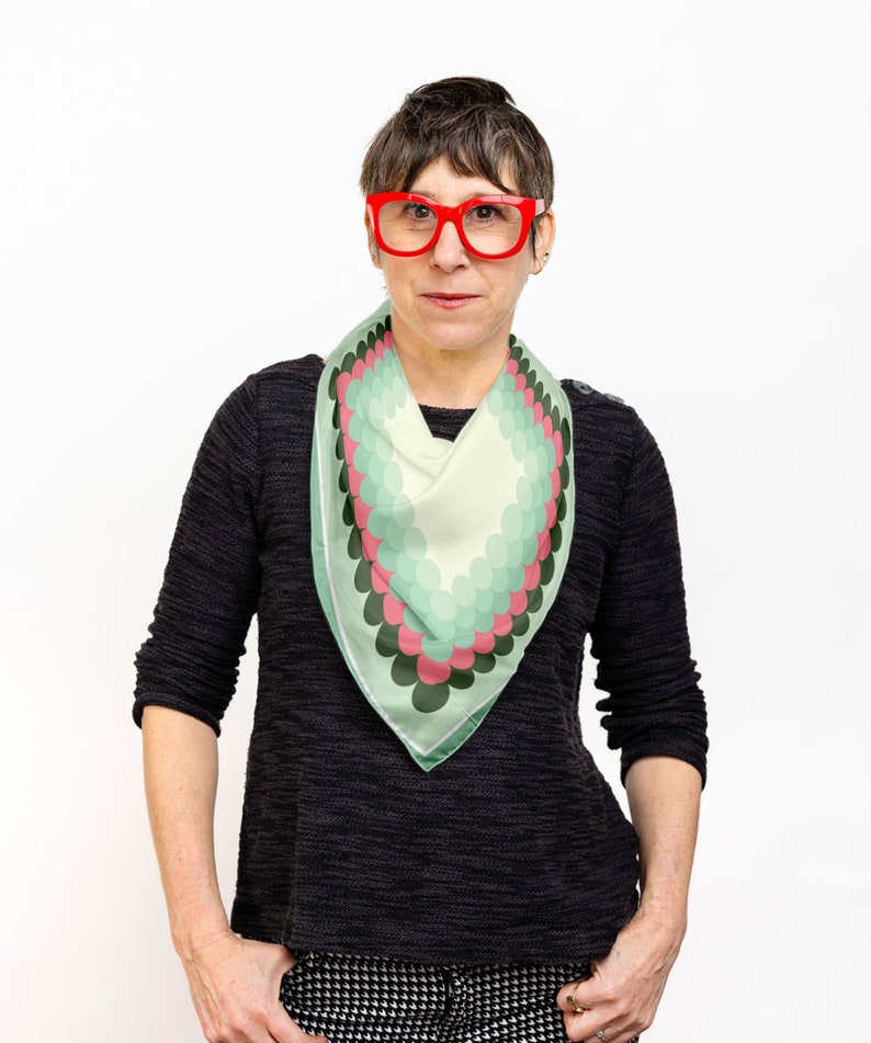 May include: A woman wearing a black sweater and black and white patterned pants. She is wearing a green, pink, and white patterned scarf and red glasses.