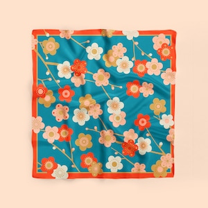 May include: A square blue silk scarf with a red border. The scarf features a repeating pattern of white, pink, and gold flowers with red centers. The flowers are arranged in a symmetrical pattern on the scarf.