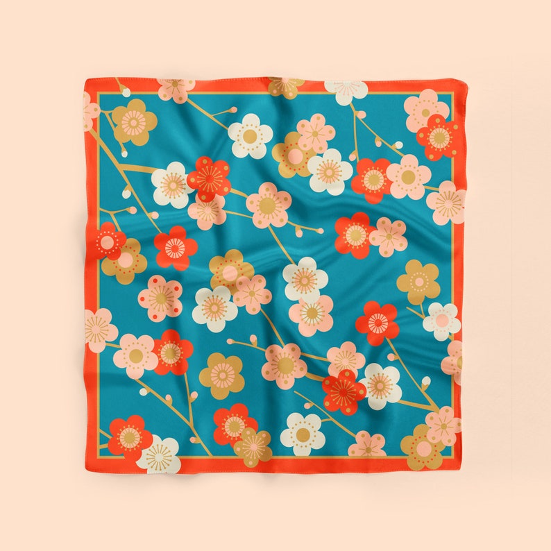 May include: A square blue silk scarf with a red border. The scarf features a repeating pattern of white, pink, and gold flowers with red centers. The flowers are arranged in a symmetrical pattern on the scarf.