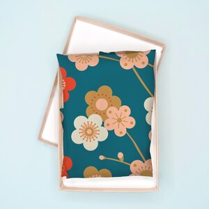 May include: A teal blue pillow with a floral pattern. The flowers are pink, white, and gold with red centers. The pillow is in a light brown box.