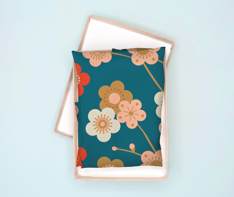 May include: A teal blue pillow with a floral pattern. The flowers are pink, white, and gold with red centers. The pillow is in a light brown box.