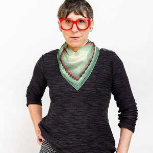 May include: A woman wearing a black sweater with a green and pink patterned scarf and red glasses.