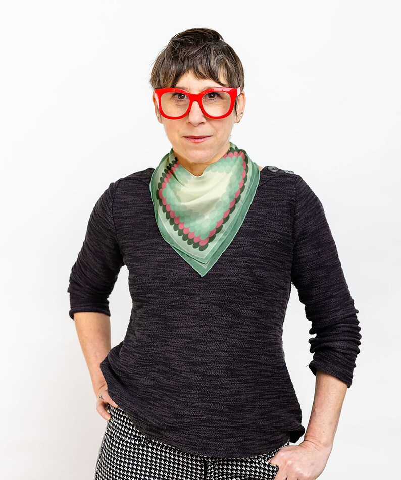 May include: A woman wearing a black sweater with a green and pink patterned scarf and red glasses.