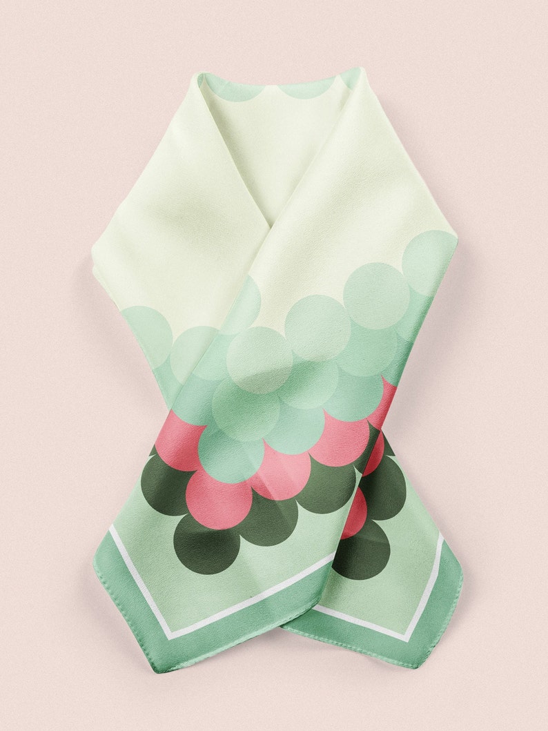 May include: A green and white silk scarf with a pattern of overlapping circles in shades of green, pink, and black. The scarf has a white border.