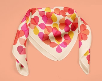 May include: A white silk scarf with a geometric pattern of pink, red, and yellow overlapping circles. The scarf is folded into a triangle shape.