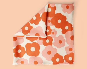 May include: A white fabric square with a repeating pattern of orange and pink flowers. The fabric is folded in half, showing the pattern on both sides.