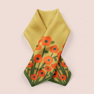 May include: Mustard yellow scarf with a floral pattern. The scarf features orange flowers with blue centers and green stems and leaves. The edges are trimmed with a dark green border. The scarf is folded and draped.