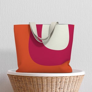 May include: A tote bag with a geometric design featuring orange, pink, and white shapes. The bag has cream-colored straps.