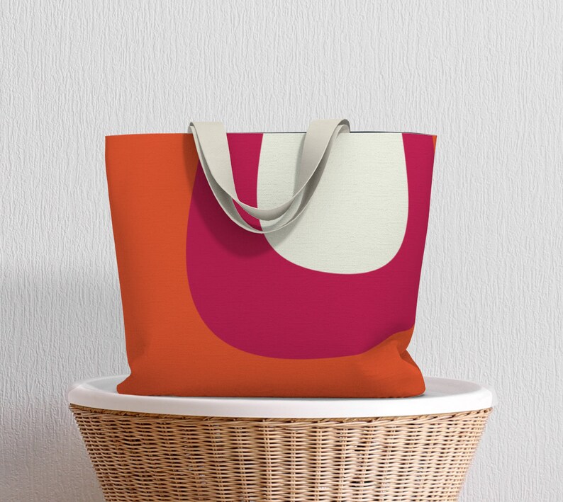 May include: A tote bag with a geometric design featuring orange, pink, and white shapes. The bag has cream-colored straps.