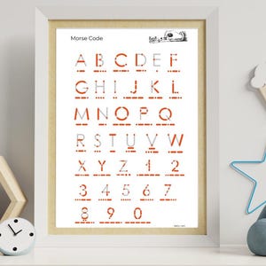Peut inclure: Un cadre affiche l'alphabet et les chiffres du code Morse en rouge et noir. L'impression est intitulée "Code Morse" et présente un personnage de dessin animé. Le cadre est posé sur une étagère blanche avec des jouets.