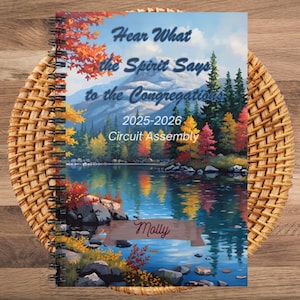 May include: A spiral-bound notebook with a scenic landscape cover featuring a lake, mountains, and colorful trees. The cover includes the text "Hear What the Spirit Says to the Congregations 2025-2026 Circuit Assembly" and the name "Molly".