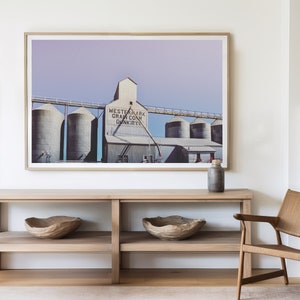 May include: A framed photograph of a grain elevator with the text "Western Mark Grain Co. Dunkirk" on the side. The photograph is hanging on a white wall above a wooden console table with two wooden bowls on the shelves.