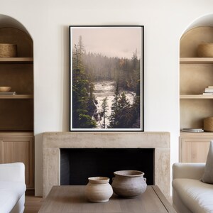 May include: A framed photograph of a misty forest scene with a river flowing through it. The photograph is hanging on a wall above a fireplace in a living room.