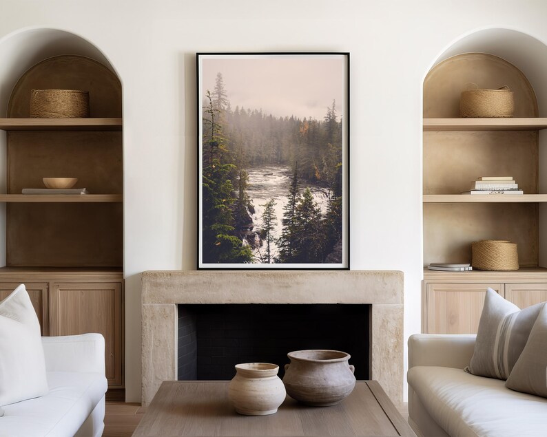May include: A framed photograph of a misty forest scene with a river flowing through it. The photograph is hanging on a wall above a fireplace in a living room.