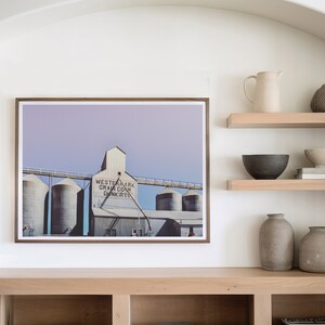 May include: A framed photograph of a grain elevator with the text "Western Mark Grain Co. Dunkirk" on the side. The photo is displayed on a shelf with other decorative items, including a pitcher, bowls, and vases.