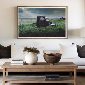 Pu&ograve; includere: Un divano bianco con cuscini marroni si trova di fronte a una fotografia incorniciata di un camion arrugginito in un campo. Un tavolino da caff&egrave; in legno con una ciotola e un vaso si trova di fronte al divano.