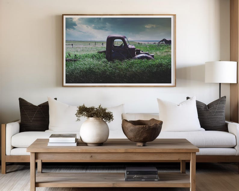 Pu&ograve; includere: Un divano bianco con cuscini marroni si trova di fronte a una fotografia incorniciata di un camion arrugginito in un campo. Un tavolino da caff&egrave; in legno con una ciotola e un vaso si trova di fronte al divano.