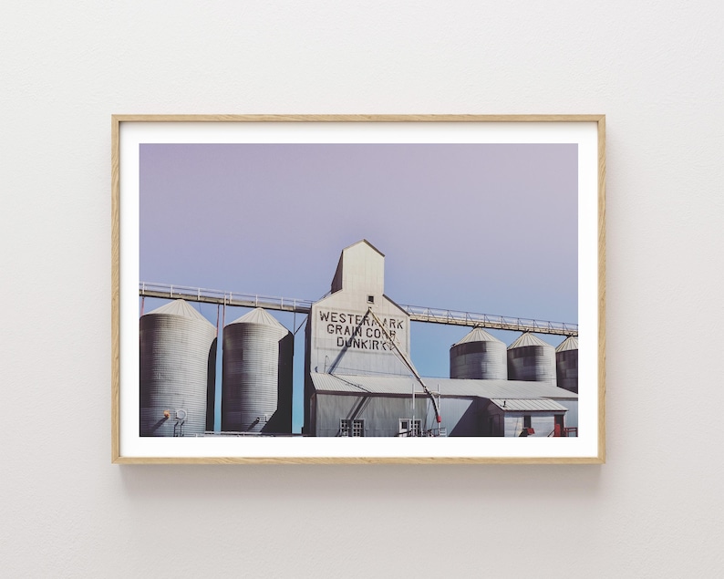 May include: A vintage photograph of a grain elevator with the text "Western Mark Grain Co. Dunkirk" on the side. The building is made of concrete and has a weathered, industrial look. The sky is a soft purple color.