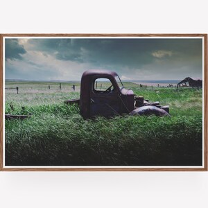 Pu&ograve; includere: Un camioncino rosso arrugginito &egrave; parzialmente immerso in un campo di erba verde alta. Il camioncino &egrave; rivolto verso il lato destro dell'immagine e la cabina &egrave; visibile. Il cielo &egrave; nuvoloso e lo sfondo &egrave; un campo di erba verde.