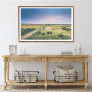 May include: A framed photograph of a white church with a steeple in a field with a road leading to it. The sky is blue and there are clouds in the distance.