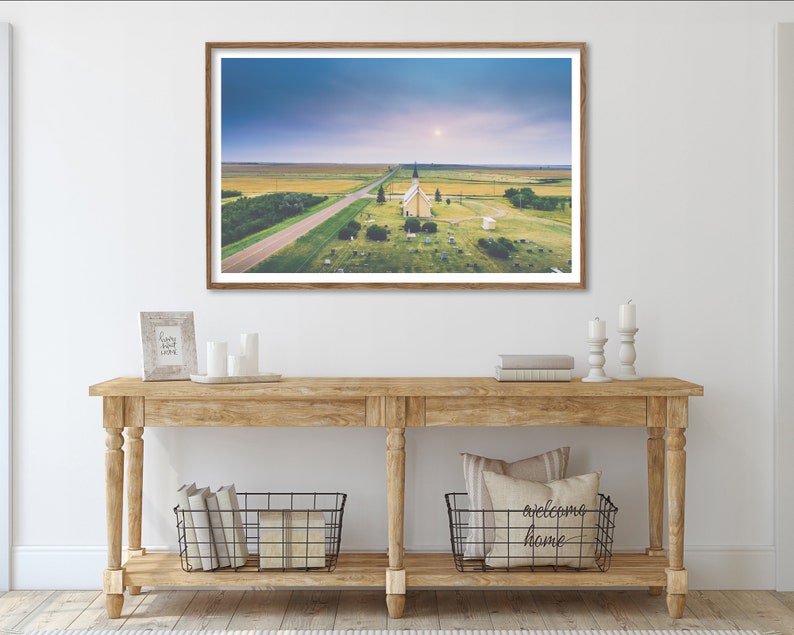 May include: A framed photograph of a white church with a steeple in a field with a road leading to it. The sky is blue and there are clouds in the distance.
