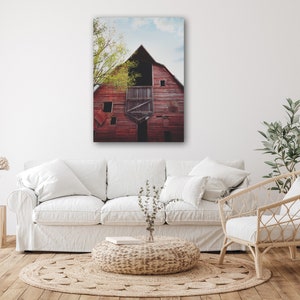 May include: A weathered red barn with a partially open door and a window. The barn is surrounded by trees and a blue sky with white clouds.