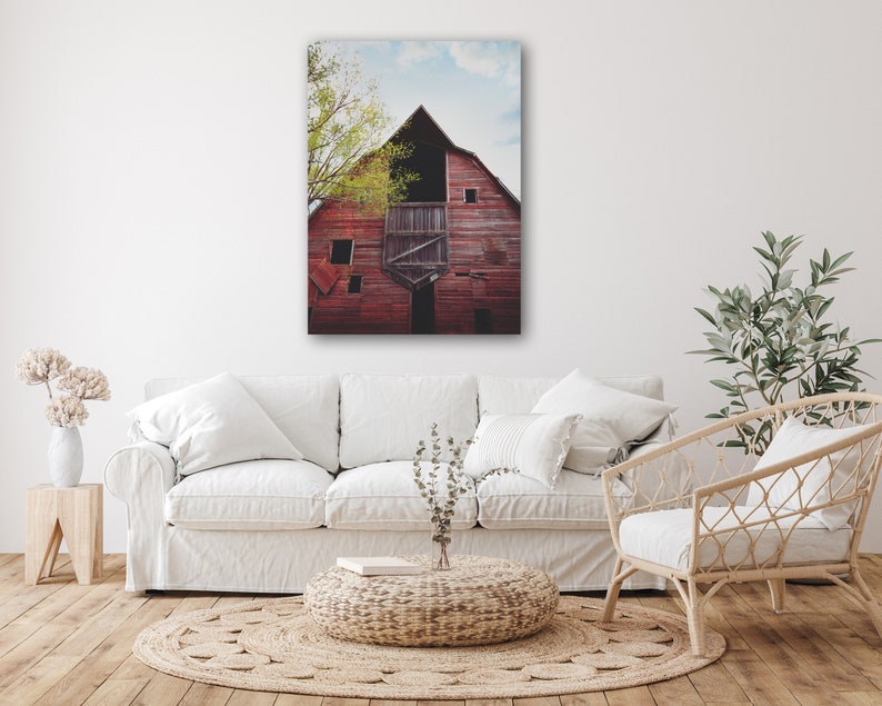 May include: A weathered red barn with a partially open door and a window. The barn is surrounded by trees and a blue sky with white clouds.