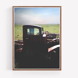 Puede incluir: Una camioneta vintage roja oxidada se encuentra parcialmente sumergida en hierba alta contra un cielo azul brillante con nubes blancas. A la camioneta le falta la parrilla delantera y el cap&oacute;, dejando al descubierto el motor.