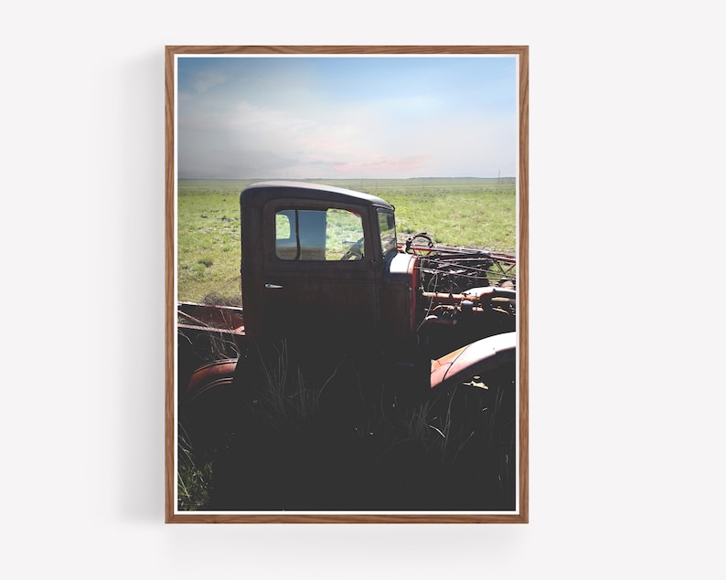 Puede incluir: Una camioneta vintage roja oxidada se encuentra parcialmente sumergida en hierba alta contra un cielo azul brillante con nubes blancas. A la camioneta le falta la parrilla delantera y el cap&oacute;, dejando al descubierto el motor.