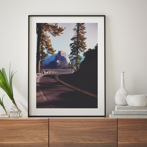 Pu&ograve; includere: Una fotografia incorniciata di una strada tortuosa che conduce alla cima di una montagna in un ambiente boschivo. La strada &egrave; fiancheggiata da alberi e la montagna &egrave; visibile in lontananza. La fotografia &egrave; in una cornice nera e appesa a un muro.