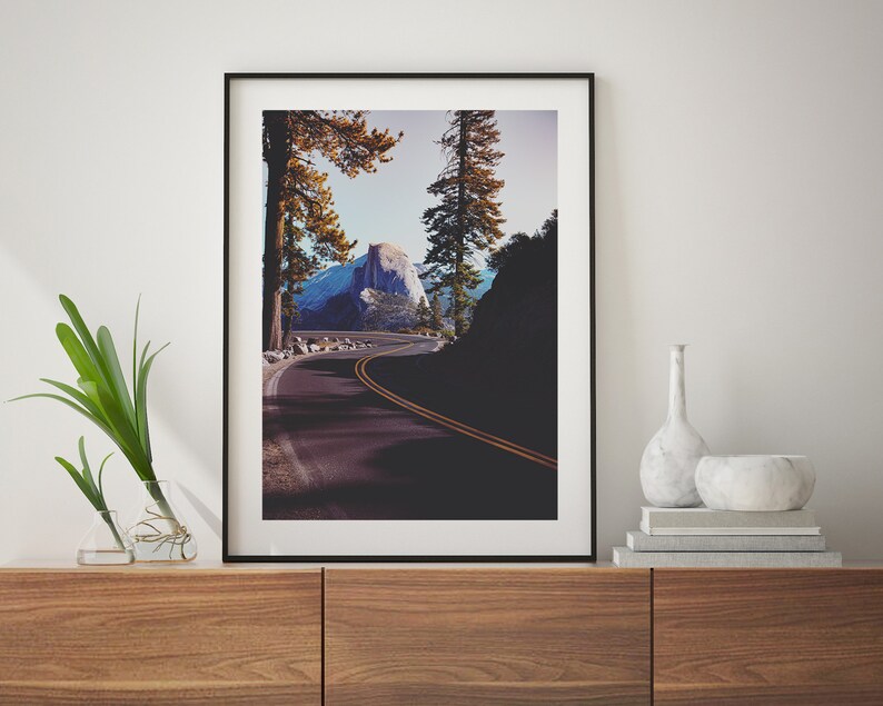 Pu&ograve; includere: Una fotografia incorniciata di una strada tortuosa che conduce alla cima di una montagna in un ambiente boschivo. La strada &egrave; fiancheggiata da alberi e la montagna &egrave; visibile in lontananza. La fotografia &egrave; in una cornice nera e appesa a un muro.