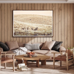 May include: A living room interior with a brown leather sofa, two matching chairs, and a wooden coffee table. A framed photograph of a group of deer in a field hangs on the wall above the sofa.