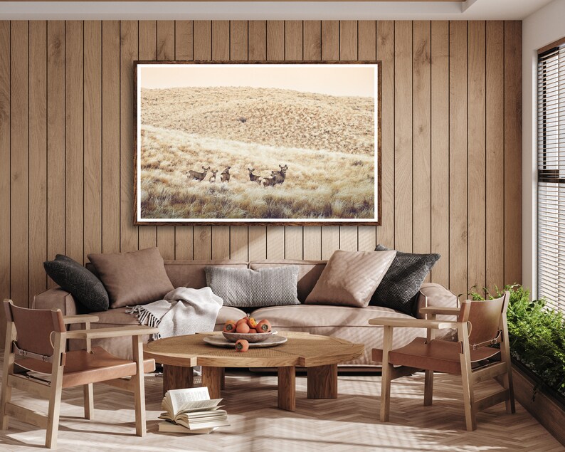 May include: A living room interior with a brown leather sofa, two matching chairs, and a wooden coffee table. A framed photograph of a group of deer in a field hangs on the wall above the sofa.