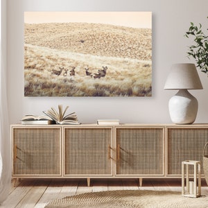 May include: A photograph of a group of deer standing in a field of tall grass. The deer are brown and have white spots. The field is a light brown color and the sky is a light blue color.