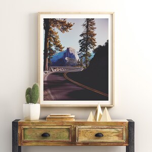 Pu&ograve; includere: Una fotografia incorniciata di una strada tortuosa che conduce alla cima di una montagna in un ambiente boschivo. La strada &egrave; fiancheggiata da alberi e la montagna &egrave; visibile in lontananza. La fotografia &egrave; in una cornice di legno chiaro ed &egrave; appesa a un muro bianco.