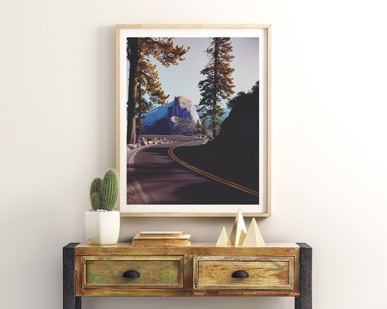 Pu&ograve; includere: Una fotografia incorniciata di una strada tortuosa che conduce alla cima di una montagna in un ambiente boschivo. La strada &egrave; fiancheggiata da alberi e la montagna &egrave; visibile in lontananza. La fotografia &egrave; in una cornice di legno chiaro ed &egrave; appesa a un muro bianco.