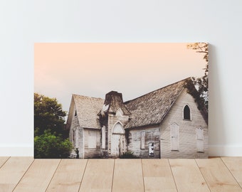 May include: A weathered, gray wooden church building with a shingled roof and a large, arched doorway. The building is surrounded by trees and a soft, pink sky.