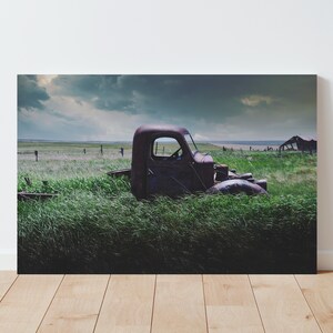 Pu&ograve; includere: Un camioncino rosso arrugginito &egrave; parzialmente immerso in un'alta erba verde. Il camioncino &egrave; rivolto verso la parte posteriore della fotocamera, e la cabina &egrave; visibile. Il cielo &egrave; nuvoloso e ci sono nuvole scure in lontananza.