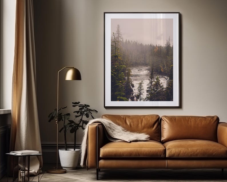 May include: A framed photograph of a misty forest scene with a river flowing through it. The photograph is in a brown frame and is hanging on a wall.