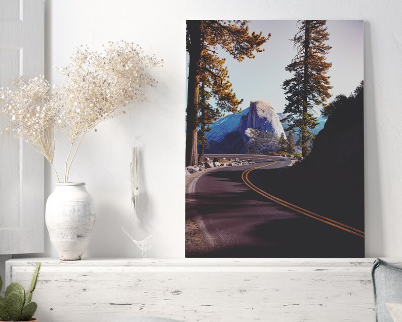 Pu&ograve; includere: Una strada tortuosa conduce a una vista di Half Dome, una formazione rocciosa di granito nel Parco Nazionale di Yosemite, in California. La strada &egrave; fiancheggiata da alberi alti e il cielo &egrave; di un blu brillante.