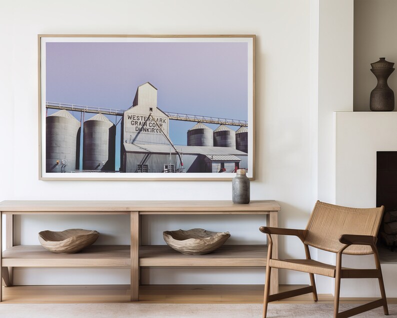 May include: A framed photograph of a grain elevator with the text "Western Mark Grain Co. Dunkirk" on the side. The photograph is hanging on a white wall above a wooden console table with two wooden bowls on the shelves.
