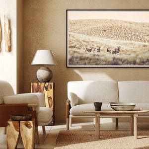 May include: A living room interior with a white sofa, two armchairs, a coffee table, and a framed photograph of a herd of deer in a field. The room is decorated with wooden accents and a neutral color palette.
