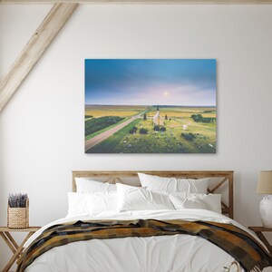 May include: An aerial view of a white church with a steeple, surrounded by a grassy field and a long, straight road leading to it. The sky is a soft blue with a few clouds.