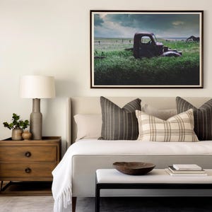 Pu&ograve; includere: Un letto bianco con una coperta bianca e un cuscino a quadri marroni e bianchi. C'&egrave; un comodino in legno con una lampada e un'immagine di un camion arrugginito in un campo sul muro.