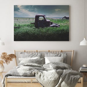 Pu&ograve; includere: Un camioncino rosso arrugginito parzialmente immerso in un'alta erba verde. Il camioncino &egrave; rivolto a destra e la cabina &egrave; visibile. Lo sfondo &egrave; un cielo nuvoloso.