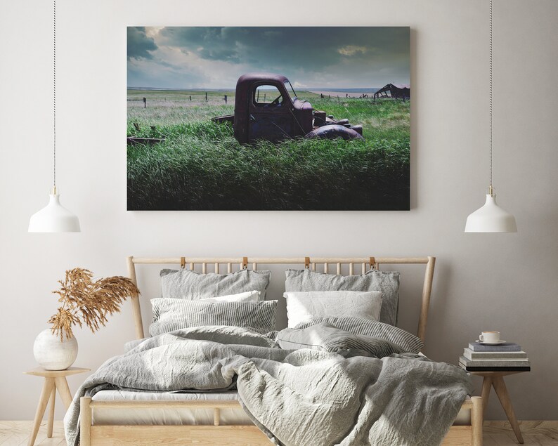 Pu&ograve; includere: Un camioncino rosso arrugginito parzialmente immerso in un'alta erba verde. Il camioncino &egrave; rivolto a destra e la cabina &egrave; visibile. Lo sfondo &egrave; un cielo nuvoloso.