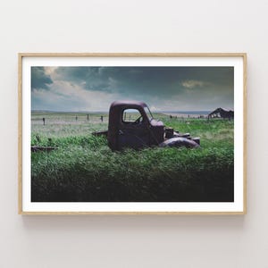 Pu&ograve; includere: Un camioncino rosso arrugginito parzialmente immerso in un'alta erba verde. Il camioncino &egrave; rivolto verso il lato destro dell'immagine. Lo sfondo &egrave; un cielo nuvoloso con un tocco di blu.