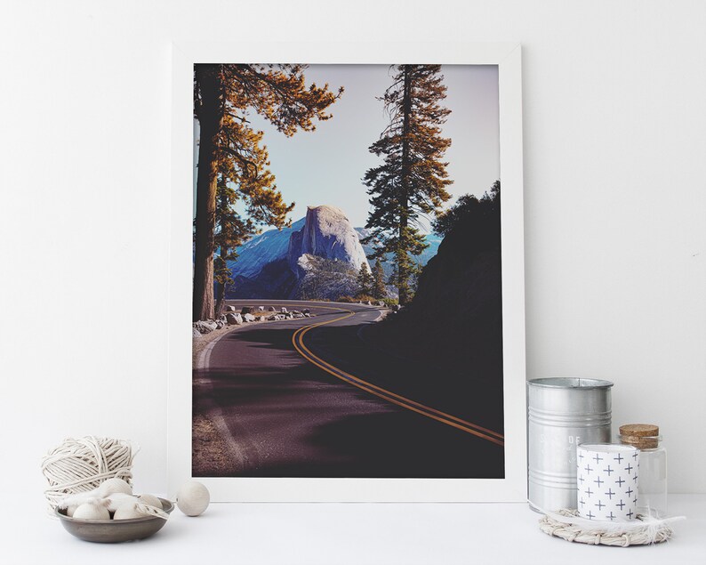 Pu&ograve; includere: Una fotografia incorniciata di una strada tortuosa che conduce a una cima di montagna nel Parco Nazionale di Yosemite. La strada &egrave; fiancheggiata da alberi e la montagna &egrave; visibile in lontananza. La foto &egrave; scattata da un angolo basso, dando allo spettatore una sensazione di prospettiva.